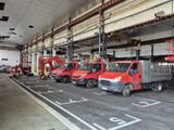 Plusieurs camions rouges sont garés dans un grand entrepôt, où se trouve un homme sur une nacelle élévatrice.
