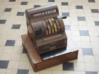 une caisse enregistreuse à l'ancienne posée sur une caisse en bois, au milieu d'un sol carrelé