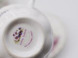 someone is holding a cup and saucer with purple flowers on it