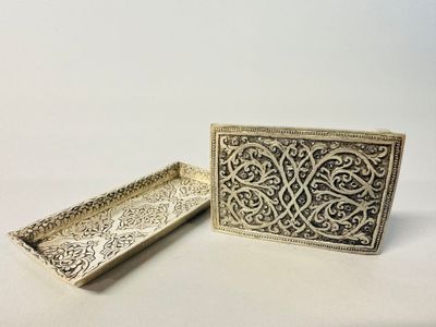 two silver trays with intricate designs on them on a white surface