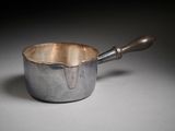 une casserole en argent avec un manche en bois posée sur une table