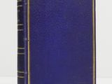 un vieux livre bleu posé sur une table à côté d'un mur blanc