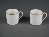 deux tasses blanches aux bords dorés sont posées sur une surface grise