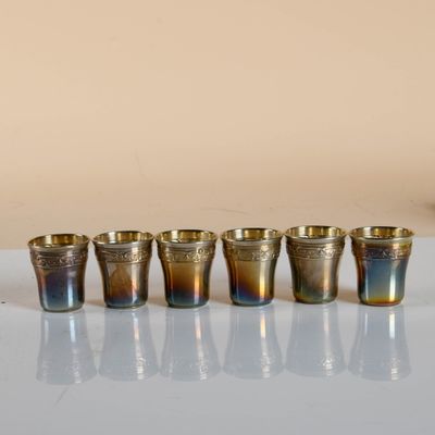 six glasses sitting on a table with a vase in front of them