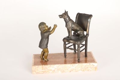 une petite statue représentant un enfant et un chien assis sur une chaise