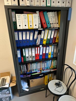 une bibliothèque remplie de classeurs et de chemises, à côté de deux chaises