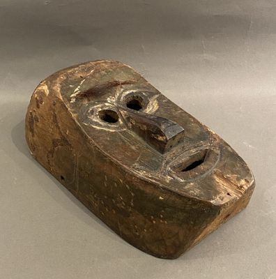 un vieux masque en bois posé sur une surface blanche