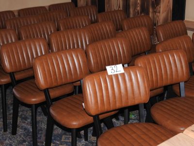 des rangées de fauteuils en cuir marron dans une salle de réunion, avec une pancarte fixée au dossier de chaque fauteuil
