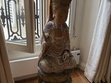 a statue of a person sitting on a stool in front of a window