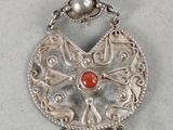 a close up of a silver pendant with a red stone on it