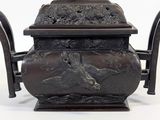 a bronze teapot with birds on it on a stand