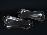 two silver trays with handles on a black background