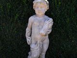 a statue of a boy standing in front of a hedge