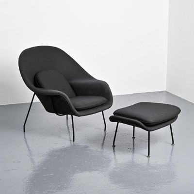 une chaise noire et un pouf dans une pièce aux murs blancs