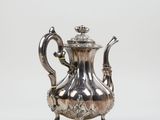 silver plated teapot with ornate decoration on stand on white background