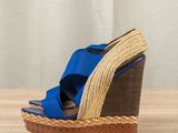 blue and brown wedged sandals on a wooden table with a curtain in the background