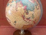 un petit globe sur un support en bois sur une surface rouge