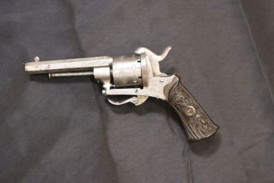 un vieux revolver avec une crosse en bois posé sur un tissu noir