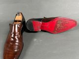 a pair of brown shoes with red soles on a gray surface