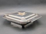 an antique silver plate with a lid on a gray surface