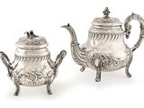 pair of antique silver teapots on stand on white background