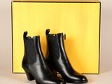 une paire de bottines en cuir noir devant une boîte jaune