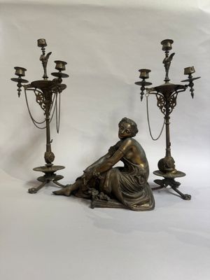 une statue représentant une femme assise par terre à côté de trois chandeliers