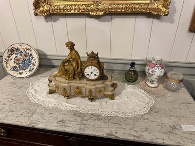 a gold clock on a marble table with a mirror above it