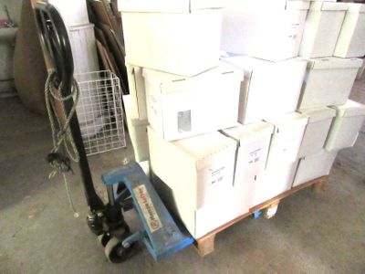 une pile de cartons posée sur une palette, à côté d'un diable