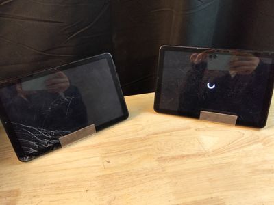 two tablet computers sitting on a table with a person taking a picture of them