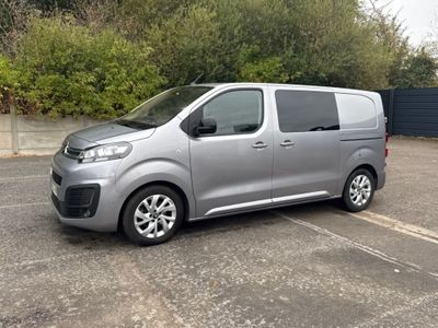 La camionnette argentée est garée sur le parking, à côté des buissons.