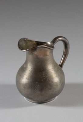une cruche ancienne en argent, dotée d'une anse incurvée, posée sur une table