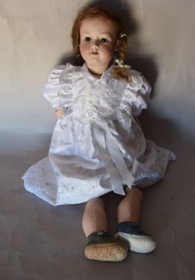 une poupée assise par terre, vêtue d'une robe blanche