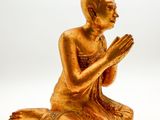 golden statue of a person sitting on the ground with their hands together