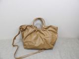beige leather handbag on a bed with a white wall in the background