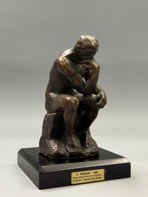 une statue en bronze représentant un homme assis sur un socle en bois