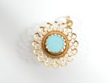 a close up of a gold and turquoise stone pendant on a white surface