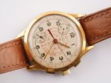 a gold watch with a brown leather strap on a white surface
