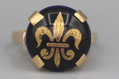 une image représentant une bague dorée et noire ornée d'une fleur de lys