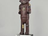 statue en bois représentant un homme tenant une pancarte, avec une inscription en dessous