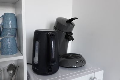 a black coffee maker sitting on top of a white shelf