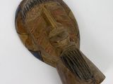 un vieux masque en bois posé sur une surface blanche, avec un fond blanc