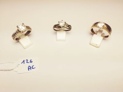 three gold rings and a diamond ring on a white surface