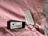 pink shirt with a tag attached to it laying on a bed