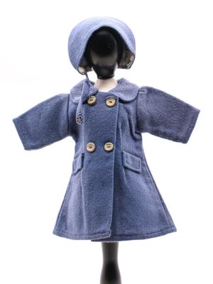 poupée vêtue d'un manteau bleu et d'un chapeau, posée sur un socle de mannequin
