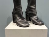 des bottines en cuir noir posées sur un socle blanc devant un mur bleu