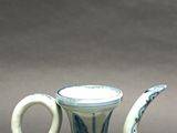 an old blue and white vase with a curved handle on a table
