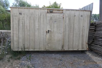 un conteneur de stockage blanc posé au milieu d'un terrain en terre battue