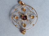 an image of a gold pendant with a red stone in the center