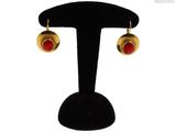 une paire de boucles d'oreilles rouges et dorées posées sur un présentoir noir